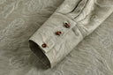 Close-up of a deep shirt cuff with three brown button-and-loop fastenings against antique sage tonal floral jacquard fabric.