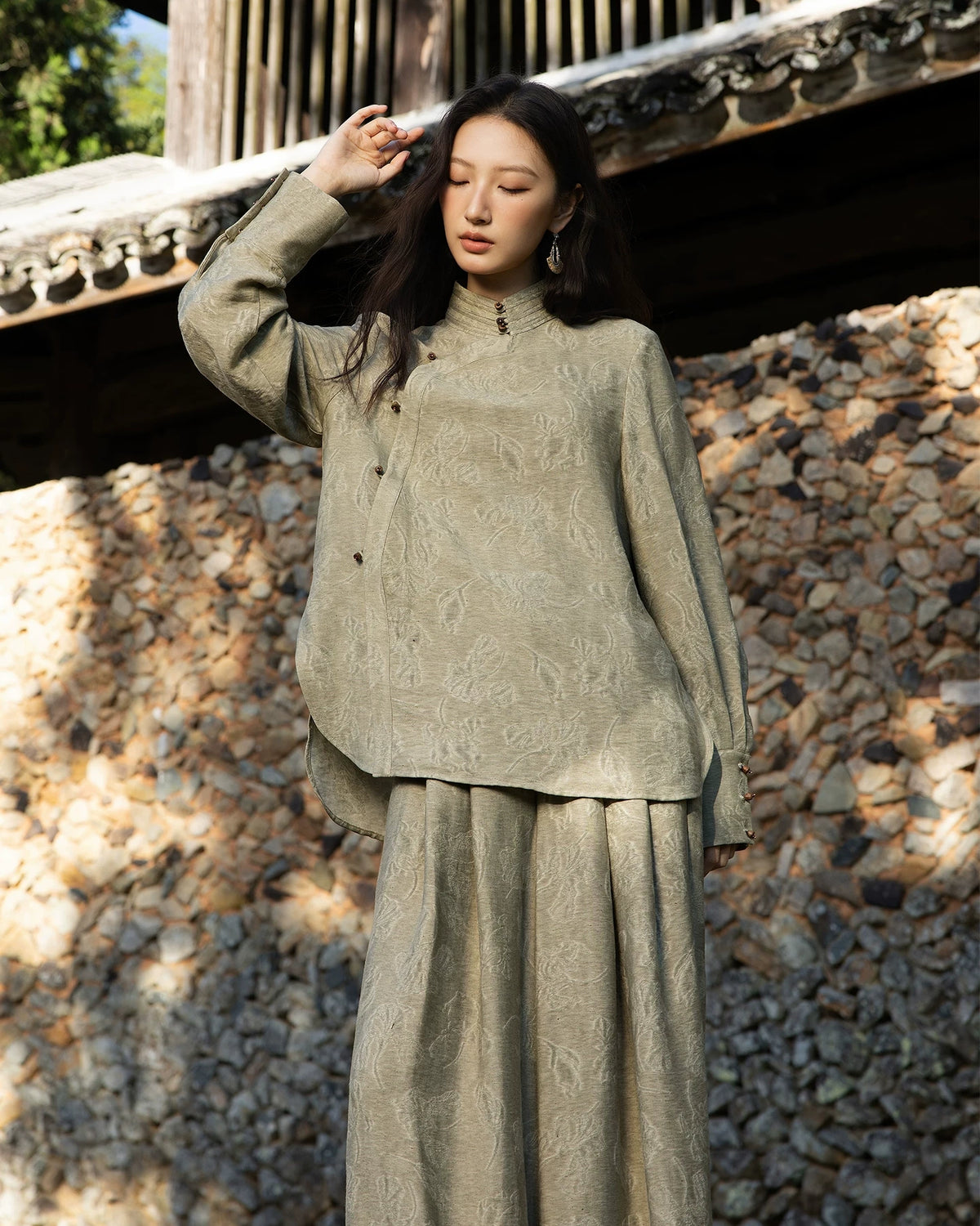 Antique sage jacquard shirt shown with one arm raised, highlighting its long sleeves, deep cuffs and curved overlapping front panel.