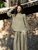 Antique sage jacquard shirt shown with one arm raised, highlighting its long sleeves, deep cuffs and curved overlapping front panel.