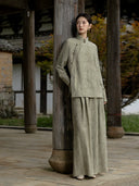Full-length view of antique sage wide-leg jacquard trousers styled with a matching asymmetric shirt and metallic shoes.