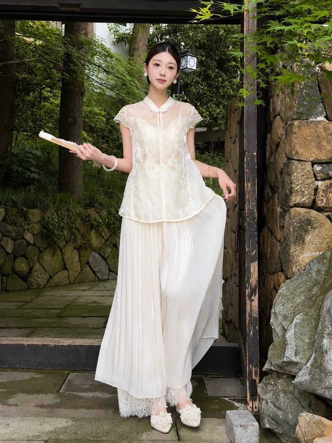 Side view of apricot cream pleated wide-leg pants with a layered lace hem, styled with a lace top and holding a fan, highlighting the relaxed and elegant fit.