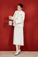 Full-length outfit featuring the beige butterfly embroidered jacket, a white pleated skirt and white heels.