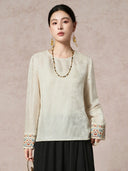 Front view of a cream white silk-blend blouse with jacquard texture and bead embroidery on the cuffs, styled with a long beaded necklace.