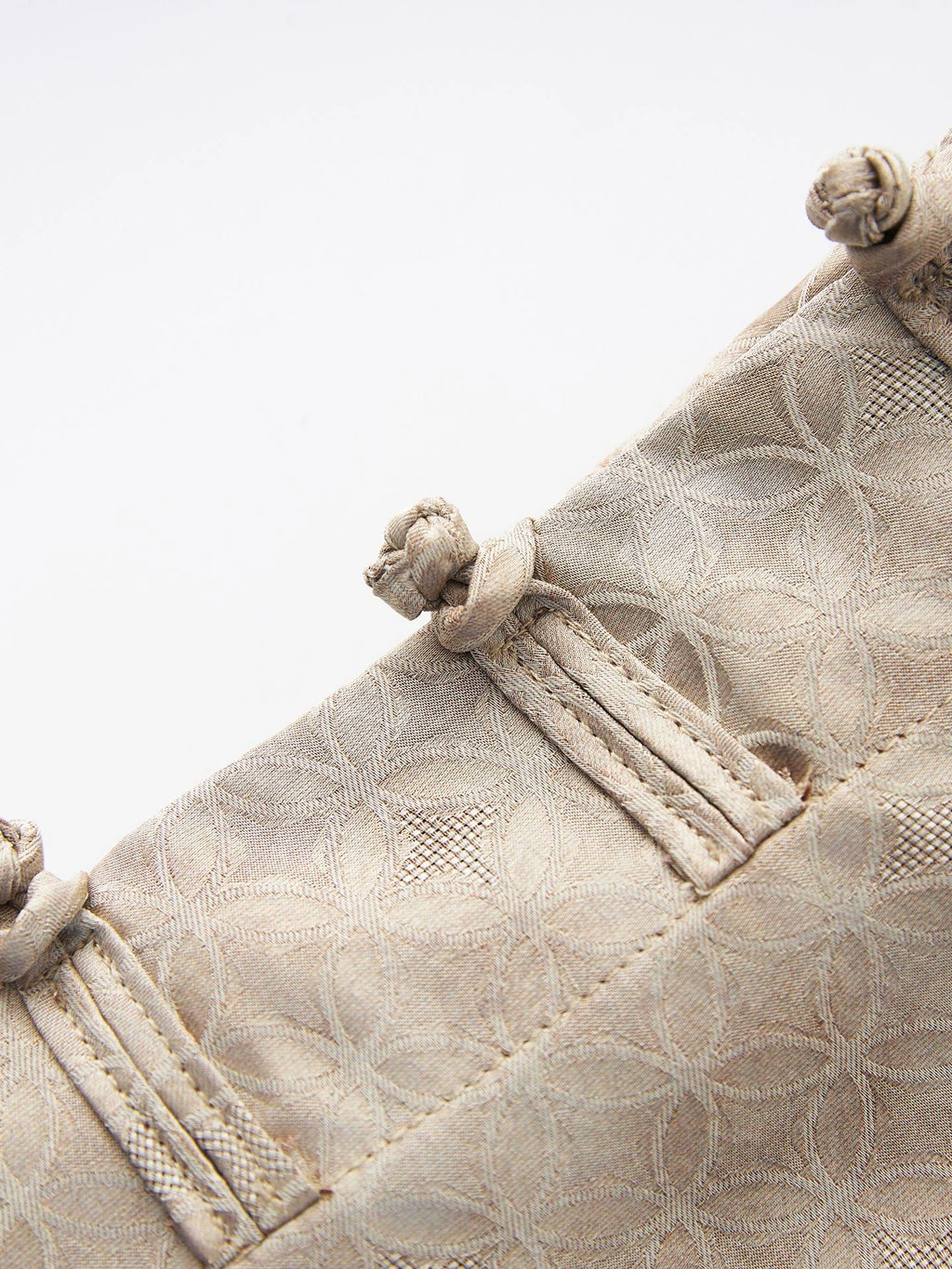 Close-up of traditional frog-button closures and geometric jacquard fabric on the beige Chinese-style vest.