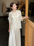Side view of a beige embroidered Cheongsam blouse with a mandarin collar, paired with a matching satin skirt, styled with a pearl necklace.