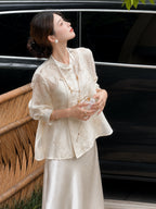 Model in a beige embroidered Cheongsam blouse and satin skirt, holding a fan and looking up, showcasing the relaxed fit and delicate embroidery.