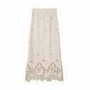 Flat lay of a beige midi skirt with floral embroidery and a scalloped lace hem, lined with 100% polyester.