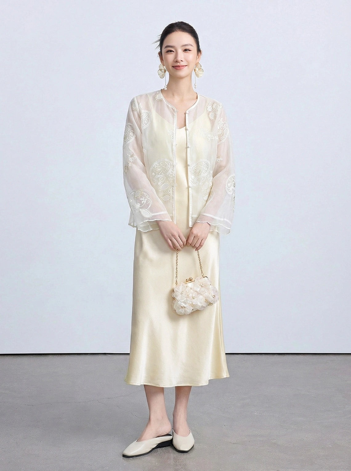 Front view of a beige New Chinese Style sheer cardigan with intricate circular embroidery and front buttons, paired with a matching satin slip dress and holding a flower-shaped bag.
