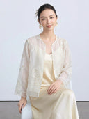Model seated in a cream sheer Tencel cardigan featuring delicate embroidery and flared sleeves, paired with a satin dress.