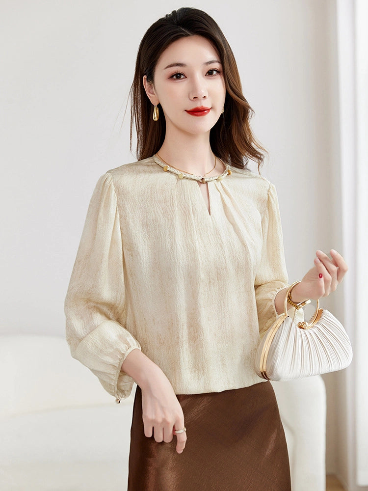 Model wearing a beige 100% mulberry silk blouse with a braided collar and puff sleeves, paired with a brown skirt and holding a white handbag.