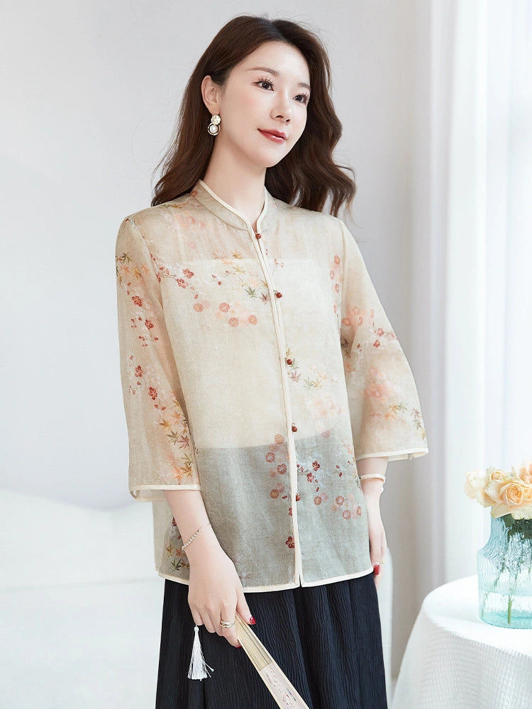 Model wearing a beige 100% silk New Chinese style blouse with a stand collar and floral print, paired with a black pleated skirt, holding a folding fan.