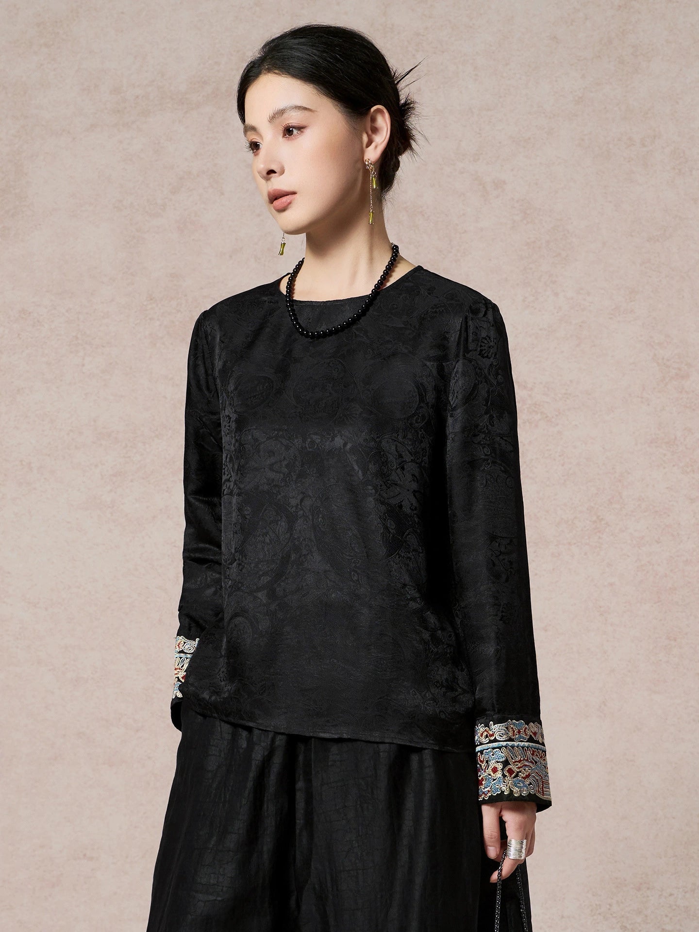 Side view of a black long-sleeve blouse with a round neck and embroidered cuffs, paired with a black skirt, highlighting the relaxed fit and traditional Chinese embroidery.