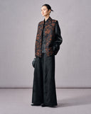 Model wearing a black and copper floral jacquard vest over a black blouse and wide-leg trousers