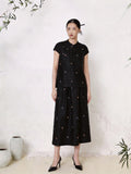 Full body shot of a black silk co-ord set featuring a short sleeve Cheongsam top with a mandarin collar and scattered colorful floral embroidery, paired with a matching A-line midi skirt with similar floral details, crafted from 100% mulberry silk.