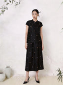 Full body shot of a black silk co-ord set featuring a short sleeve Cheongsam top with a mandarin collar and scattered colorful floral embroidery, paired with a matching A-line midi skirt with similar floral details, crafted from 100% mulberry silk.