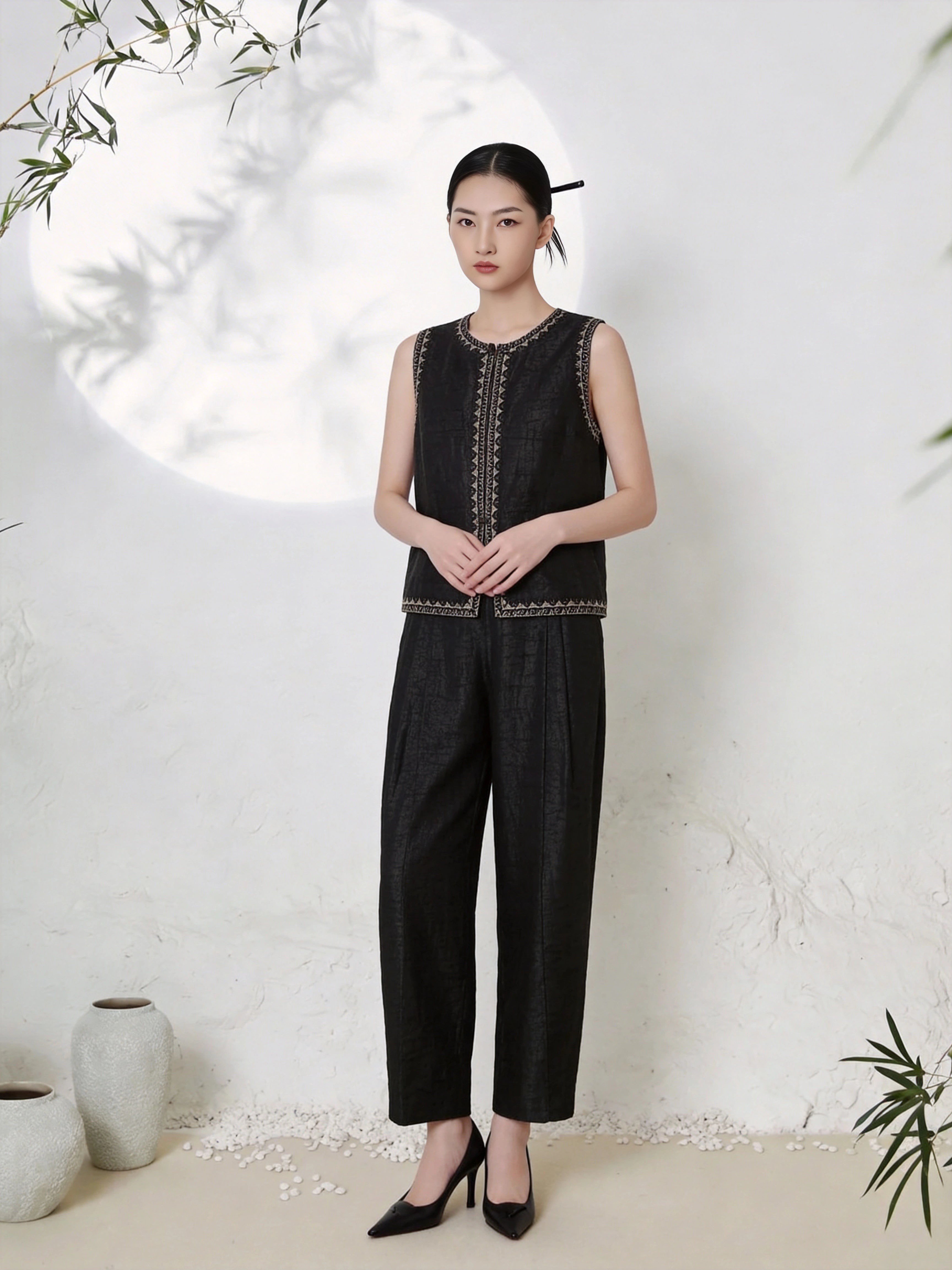 Full body shot of a black silk co-ord set featuring a sleeveless vest top with gold geometric embroidery along the neckline, center front, and hem, paired with matching straight-leg trousers, crafted from 100% mulberry silk.