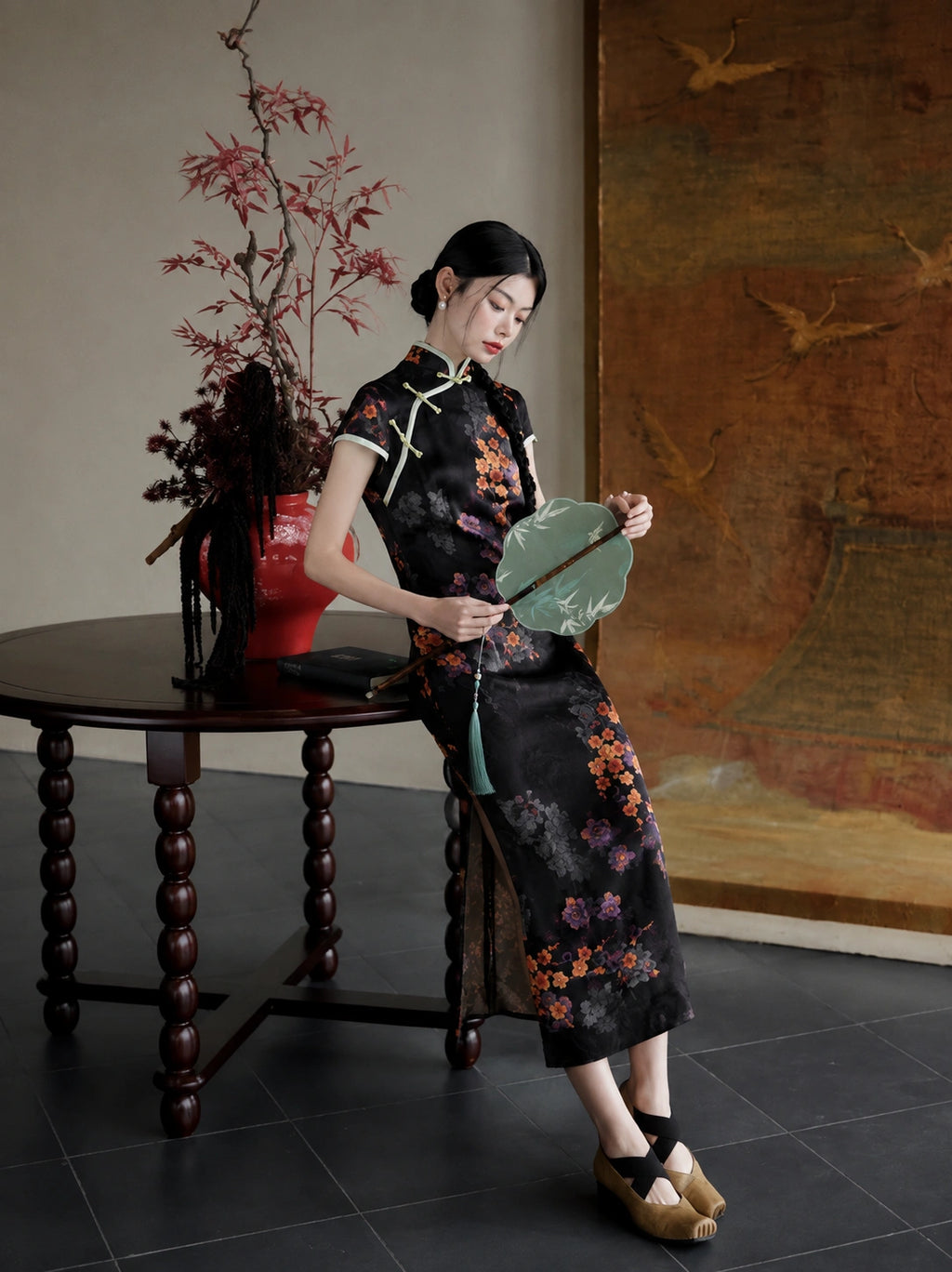 Upper-body close-up of a black floral rayon jacquard qipao with diagonal front closure, mandarin collar, and green piping.