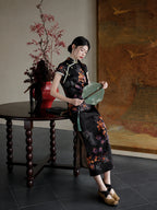 Upper-body close-up of a black floral rayon jacquard qipao with diagonal front closure, mandarin collar, and green piping.