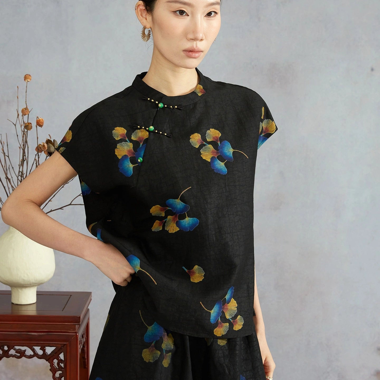 Model wearing a black mulberry silk top with multicolor ginkgo leaves, cap sleeves and Chinese-style button closures.