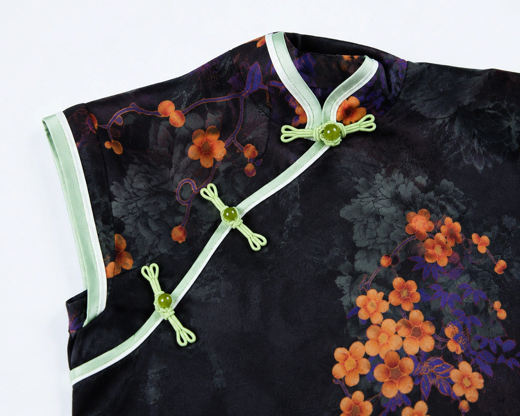 Close-up of the diagonal placket on a black jacquard qipao with pale green trim and traditional knot buttons.