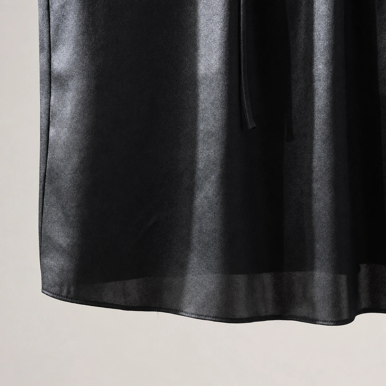 Close-up of the subtle tonal texture, sheen and lightweight hem of the black silk blouse
