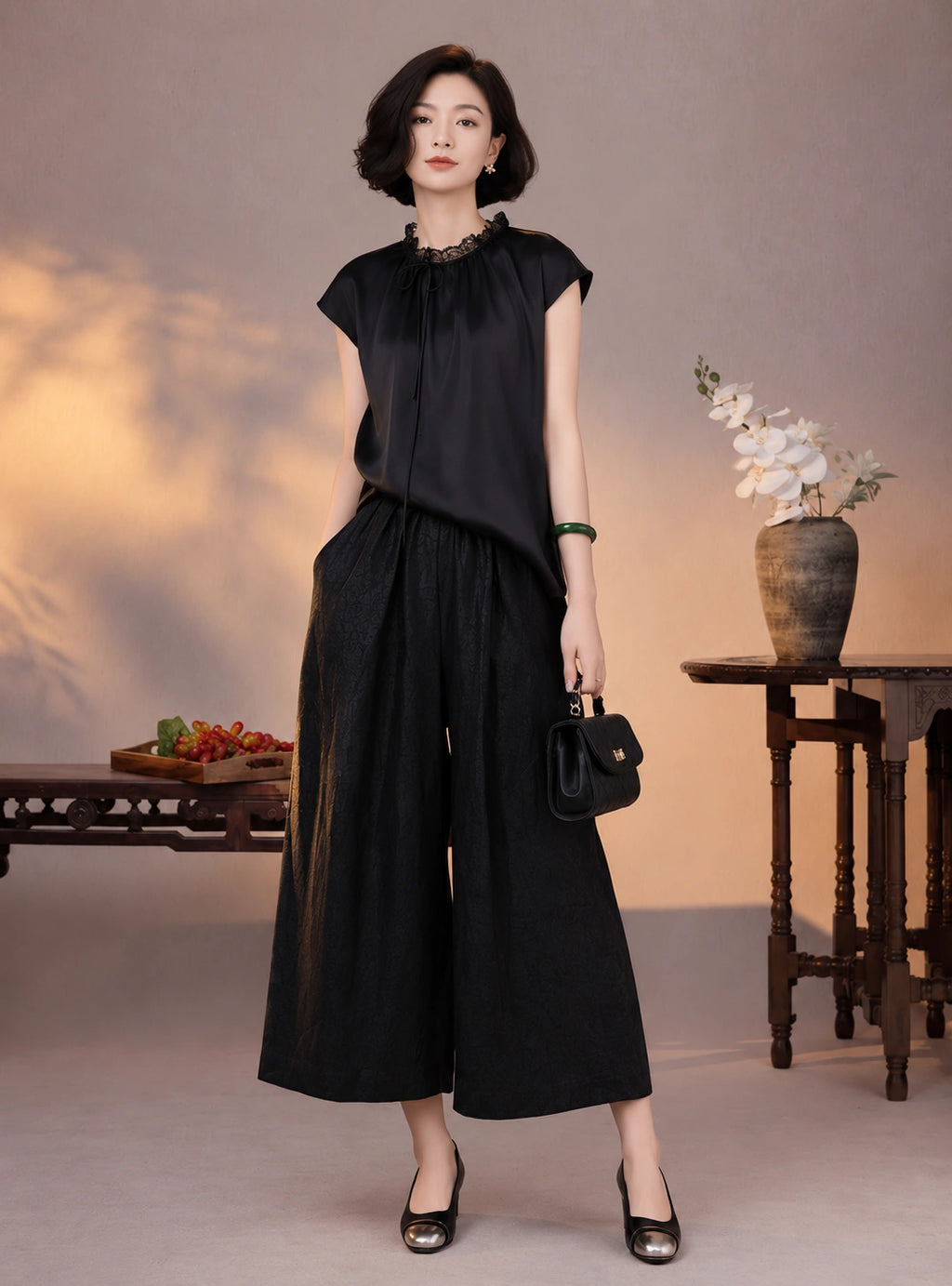 Woman wearing a black mulberry silk cap-sleeve blouse with lace trim and matching wide-leg pants
