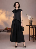 Woman wearing a black mulberry silk cap-sleeve blouse with lace trim and matching wide-leg pants
