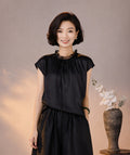 Front view of a black silk blouse with cap sleeves, a gathered neckline and delicate lace trim