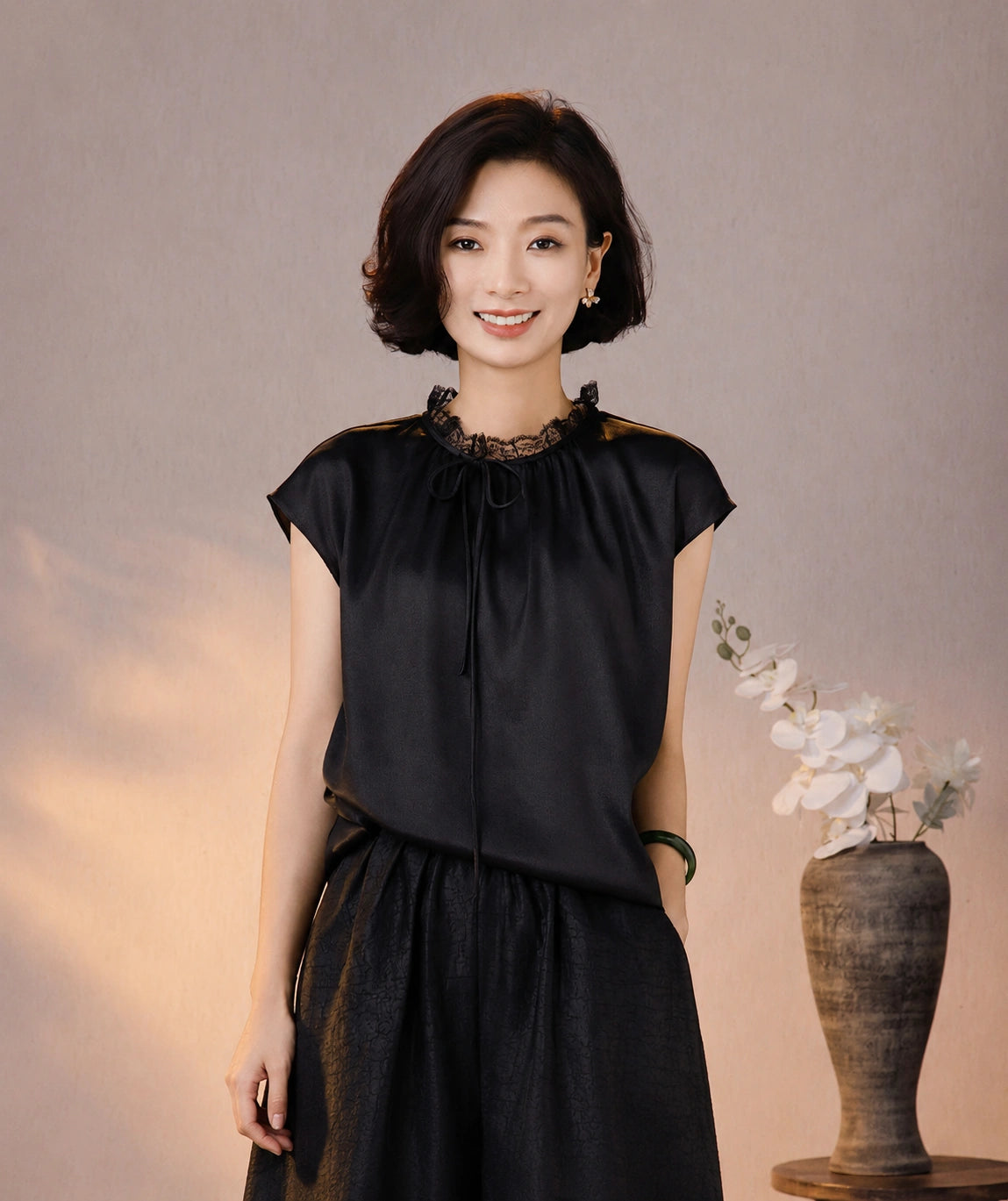 Front view of a black silk blouse with cap sleeves, a gathered neckline and delicate lace trim