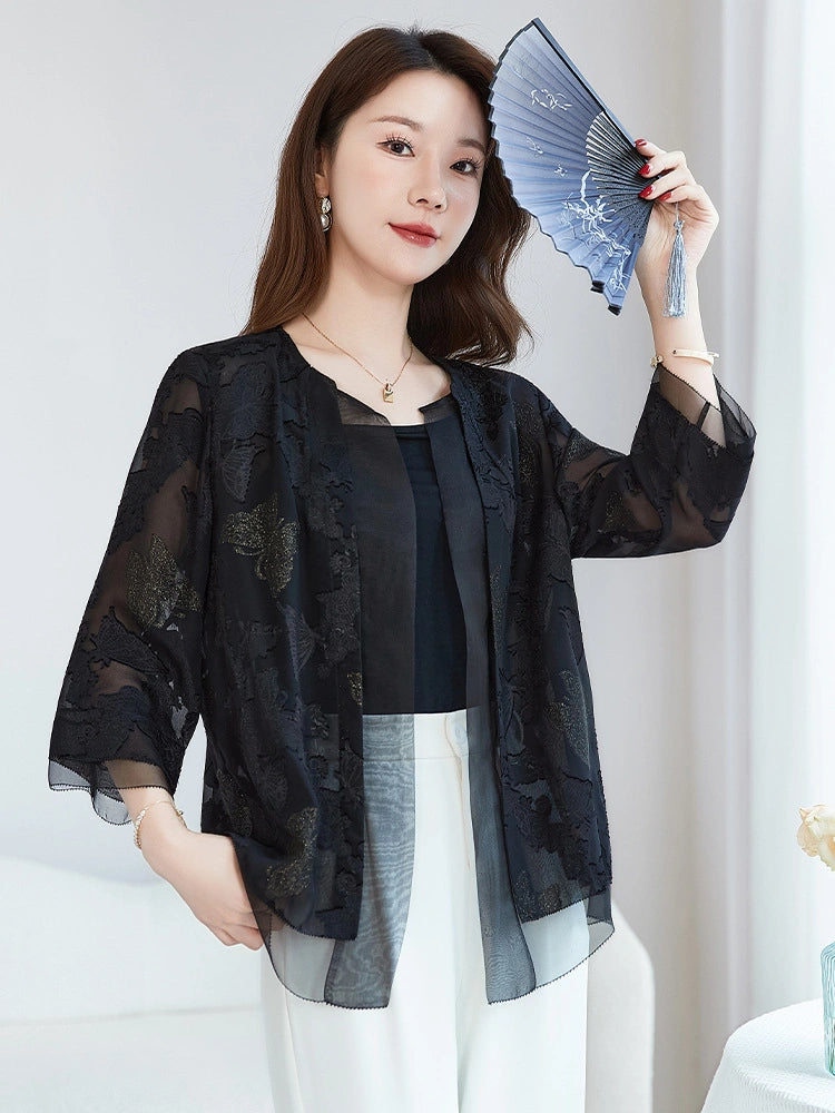 Model wearing a black sheer silk embroidered cardigan, holding a blue fan, paired with white trousers, highlighting the sophisticated New Chinese style.