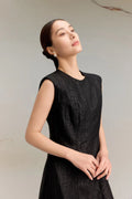 Close-up of a black silk dress with a round neckline and textured jacquard finish, highlighting the luxurious sheen and soft drape of the premium silk fabric.