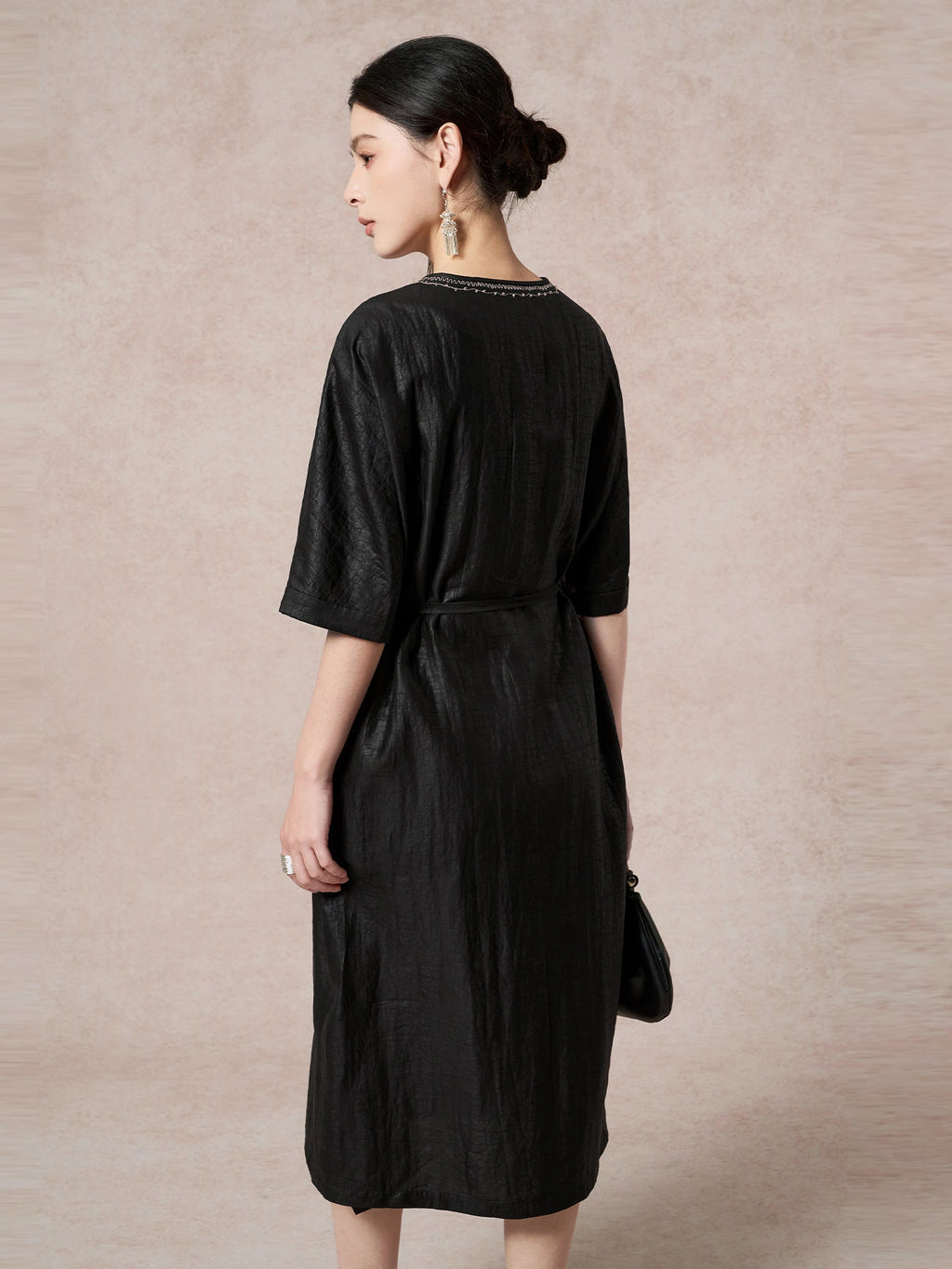 Back view of a black 100% mulberry silk dress with a round neckline, short sleeves, and a tied waist, highlighting the elegant drape and subtle texture.