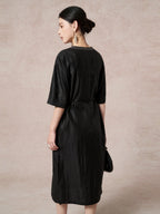Back view of a black 100% mulberry silk dress with a round neckline, short sleeves, and a tied waist, highlighting the elegant drape and subtle texture.