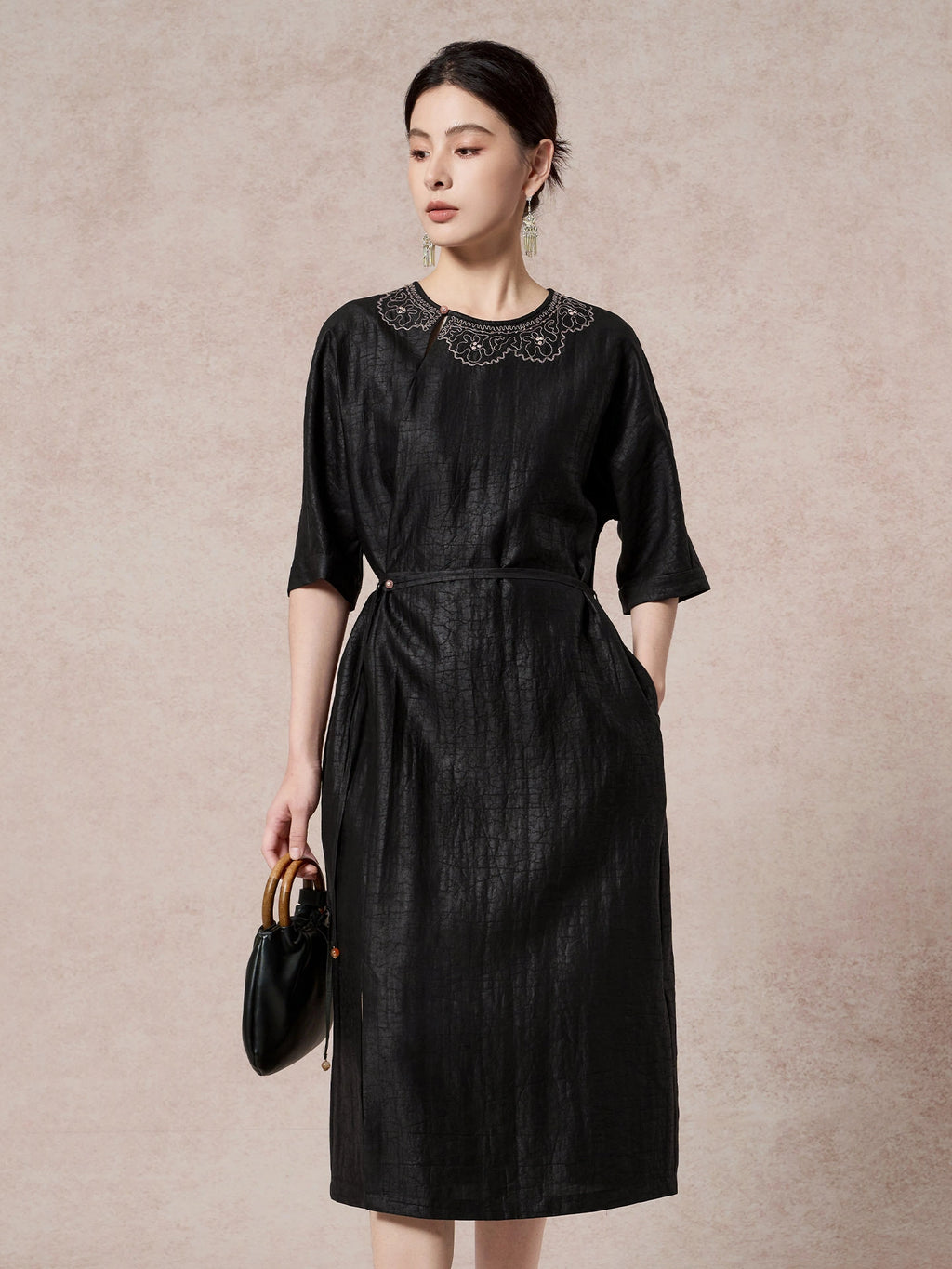 Model wearing a black silk dress with a relaxed fit and delicate embroidery, holding a black handbag, showcasing the elegant silhouette.