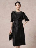 Front view of a black silk dress featuring intricate scalloped embroidery on the chest, a round neckline, and a side tie waist detail.