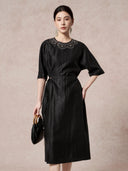 Front view of a black silk dress featuring intricate scalloped embroidery on the chest, a round neckline, and a side tie waist detail.