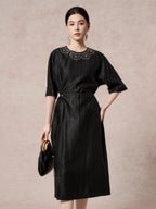Front view of a black silk dress featuring intricate scalloped embroidery on the chest, a round neckline, and a side tie waist detail.