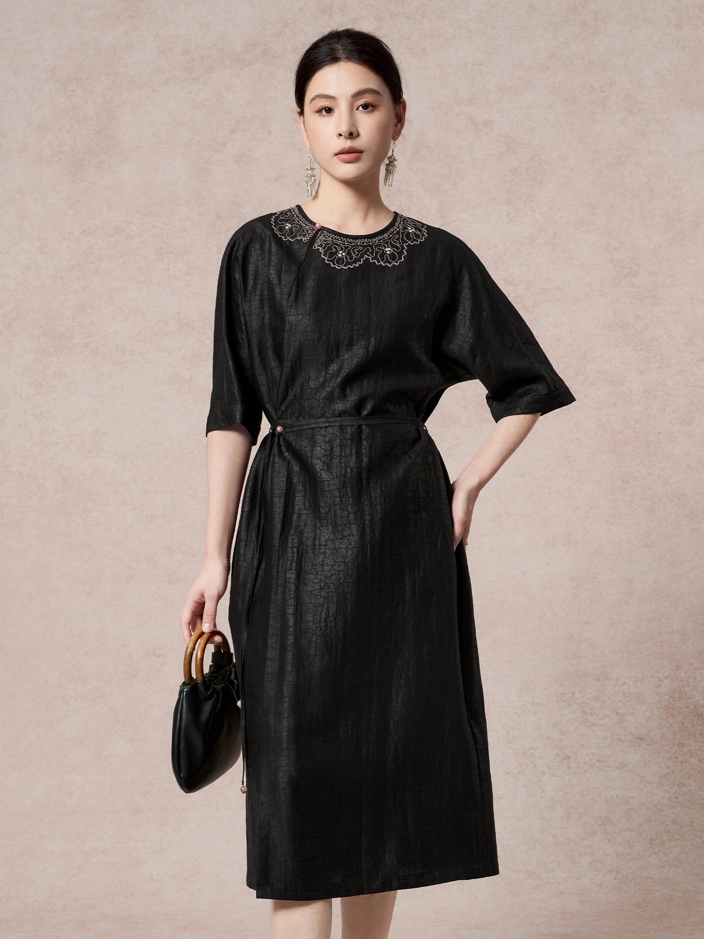 Front view of a black silk dress featuring intricate scalloped embroidery on the chest, a round neckline, and a side tie waist detail.
