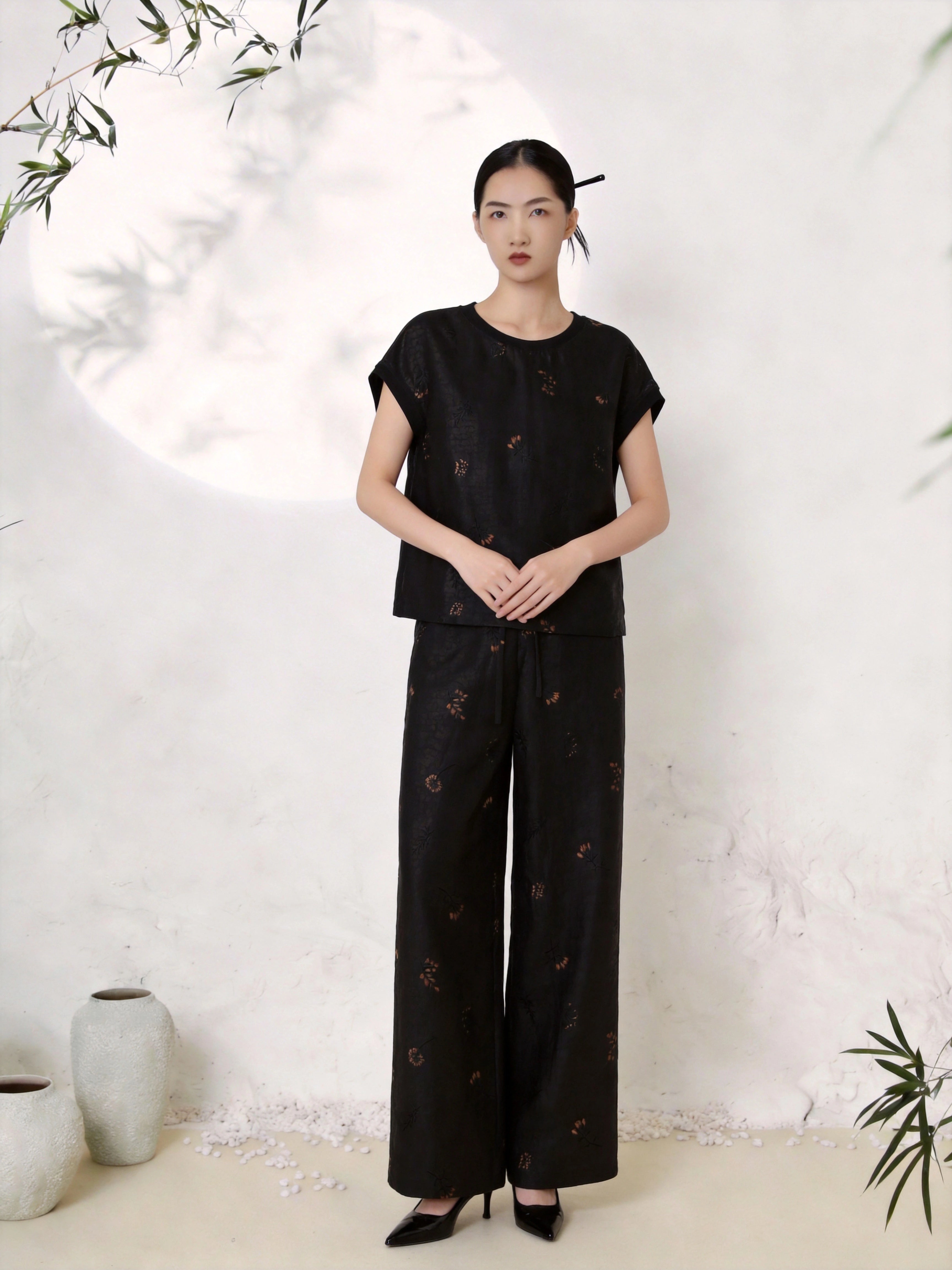Full body shot of a black silk co-ord set featuring a round neck short sleeve blouse with scattered copper-gold floral embroidery, paired with matching wide-leg palazzo trousers, crafted from 100% mulberry silk.