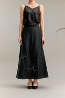 Black silk A-line maxi skirt with green and white abstract embroidery at the hem, crafted from 100% mulberry silk, paired with a black camisole.