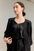 Close-up of a black silk jacket top with three-quarter sleeves, delicate lace embroidery along the edges, and a tie-front closure, featuring a V-neckline and luxurious textured silk fabric.