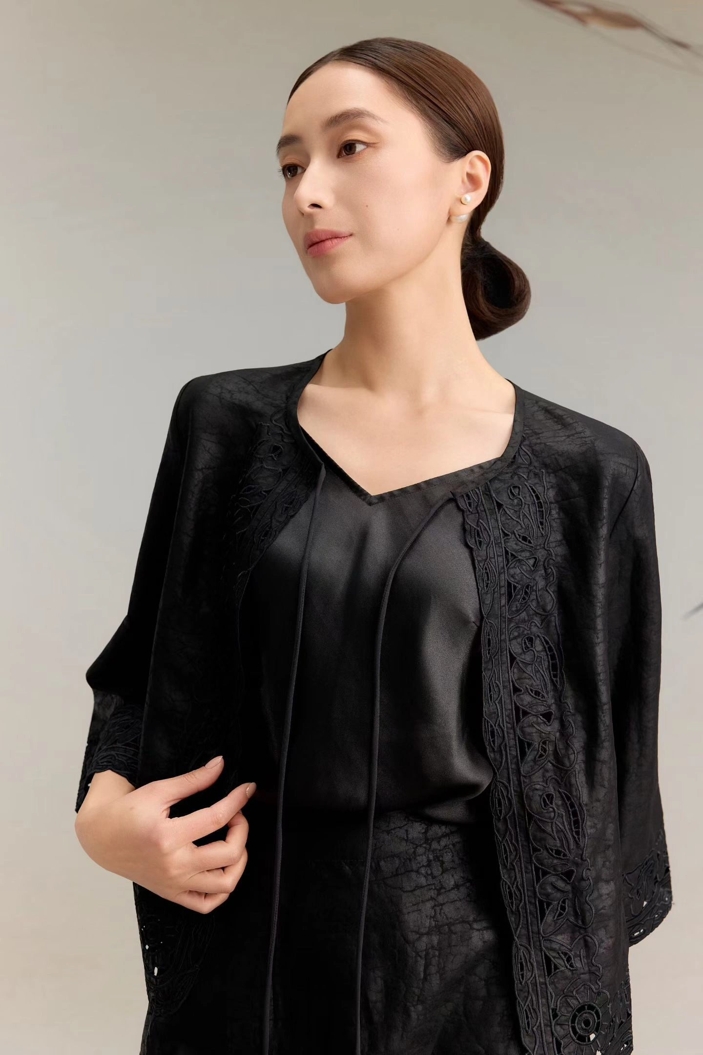 Close-up of a black silk jacket top with three-quarter sleeves, delicate lace embroidery along the edges, and a tie-front closure, featuring a V-neckline and luxurious textured silk fabric.