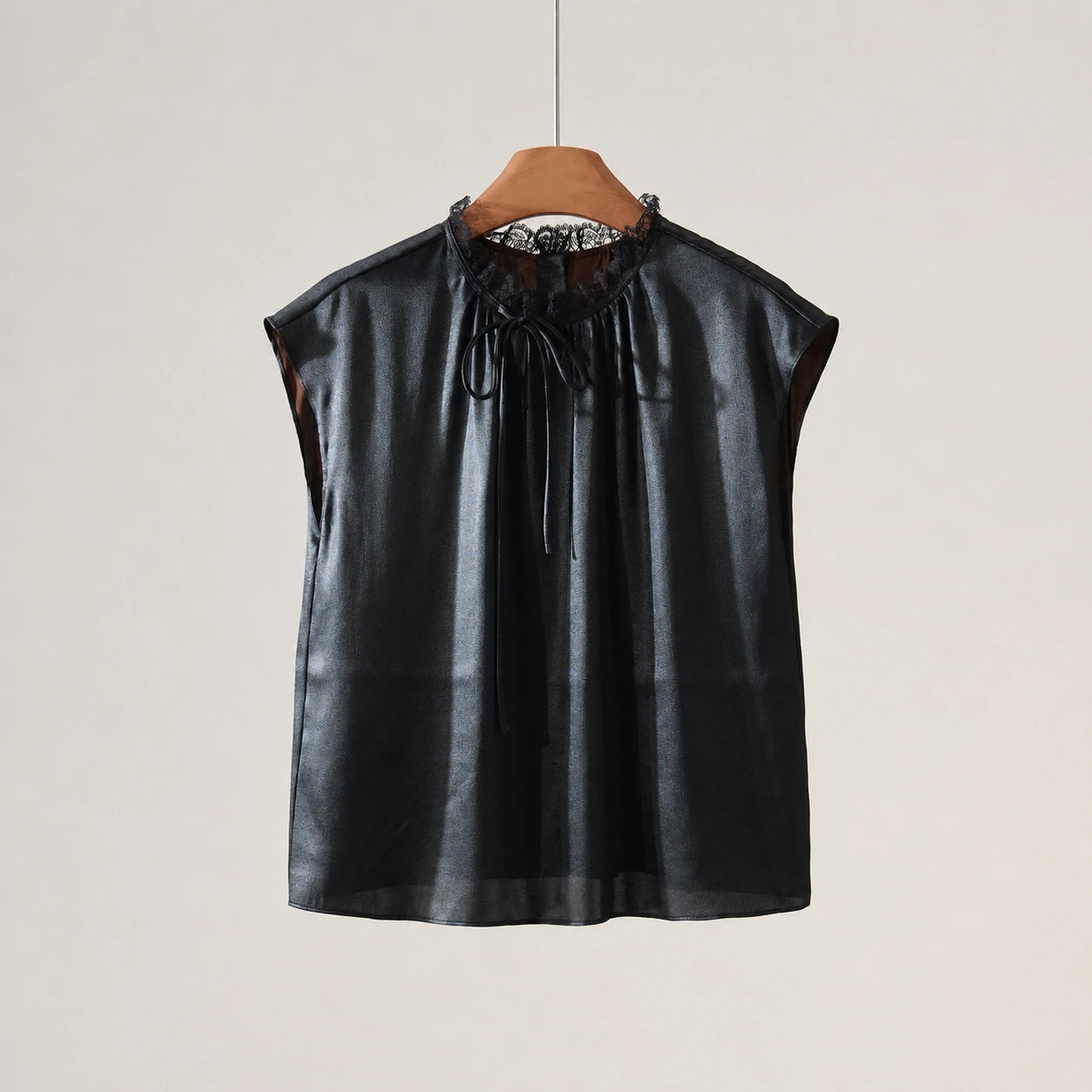 Front product view of a black silk cap-sleeve blouse with a lace-trimmed neckline and self-tie