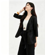 Side view of a black silk blouse with a V-neck and tied waist, featuring a subtle floral jacquard pattern, crafted from 100% mulberry silk, worn with a white camisole and black trousers.