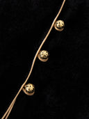Close-up of gold-toned patterned buttons, fabric loops and tan piping against black velvet.