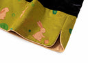 Close-up of pink rabbit motifs, floral jacquard texture and tan piping on the golden olive hem.