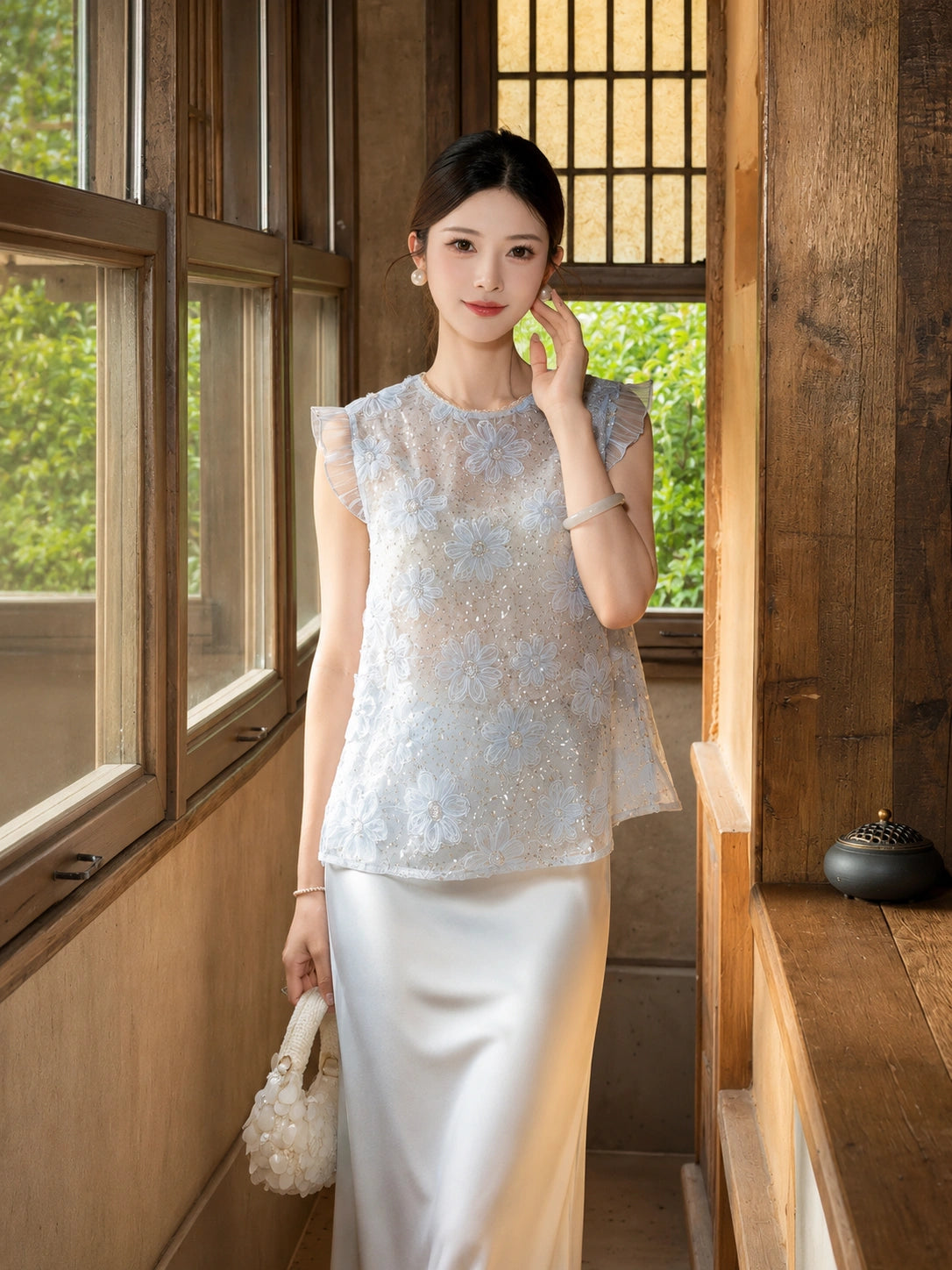 Front view of a light blue sleeveless top with 3D floral embroidery and shiny sequins, paired with a white satin skirt, 100% polyester.