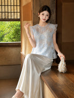 Sitting model in a light blue floral sequin top with ruffle sleeves, holding a white shell bag, showcasing the elegant 100% polyester fabric.