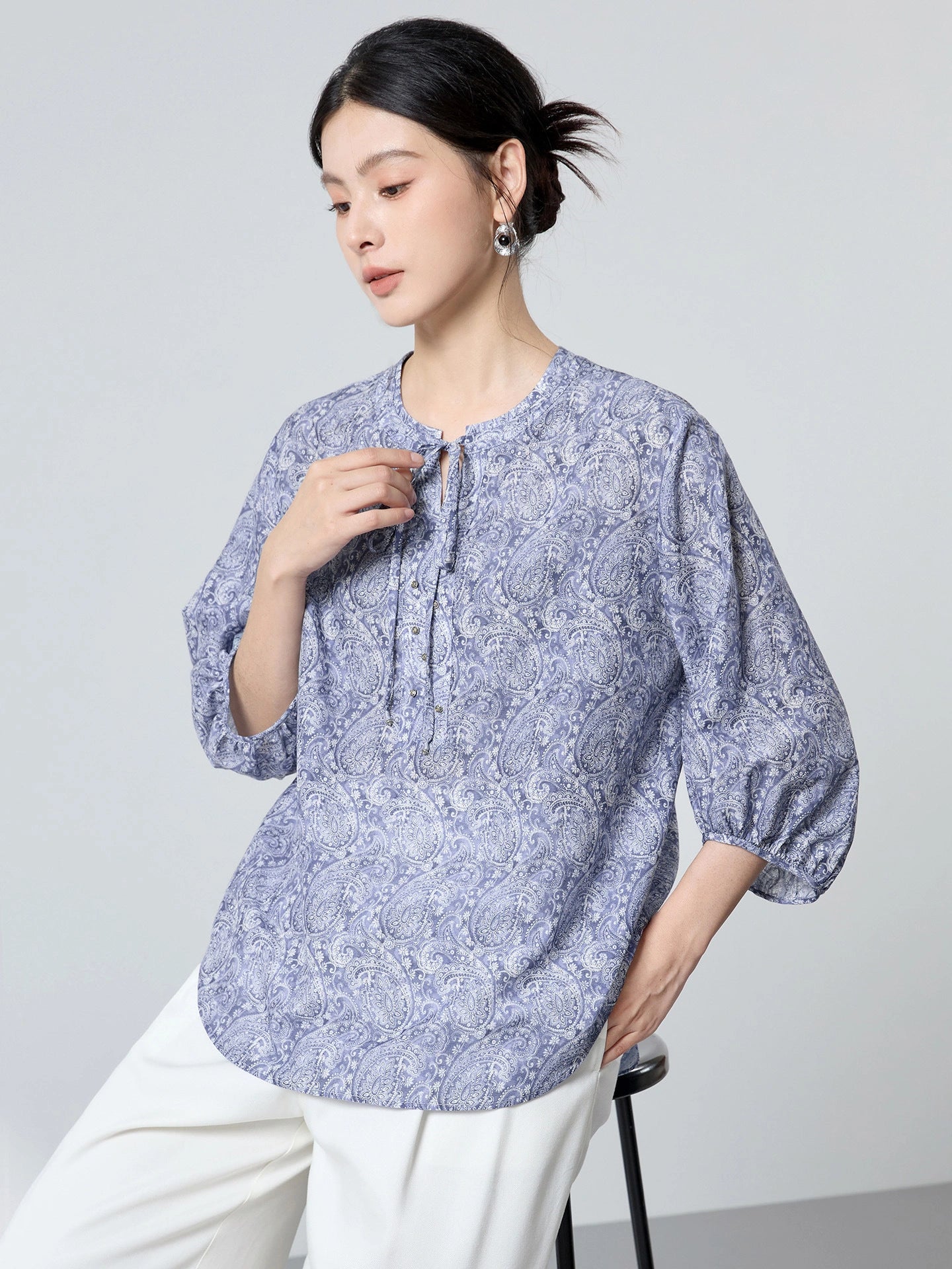 Close-up of a blue paisley print cotton-silk blouse showing the tie-neck detail, delicate buttons, and elegant drape.