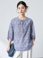 Front view of a blue paisley print cotton-silk top with a round neckline, tie-front detail, and buttoned placket, featuring a relaxed silhouette.